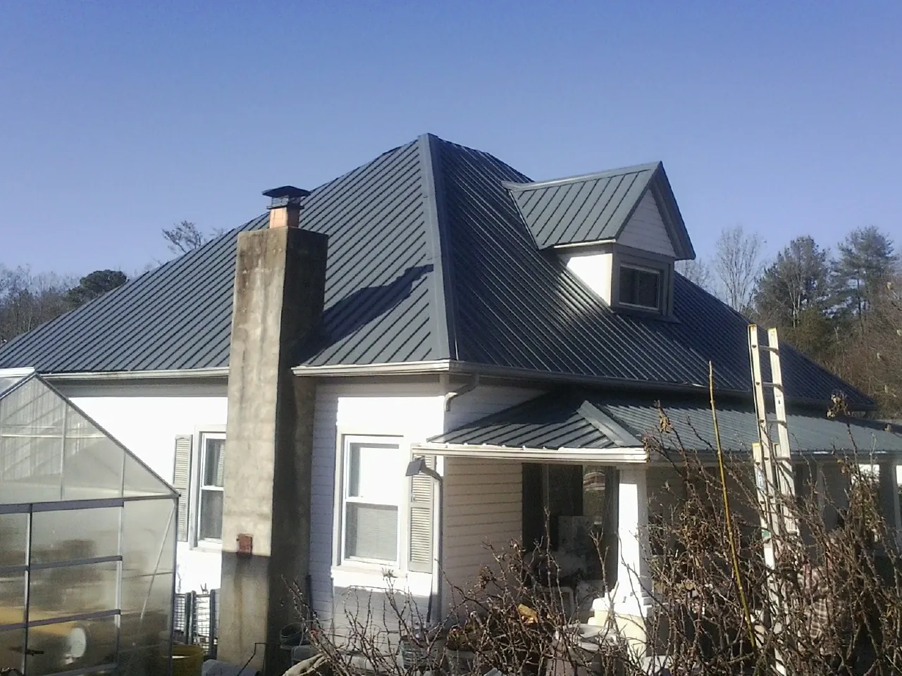 Dark blue standing seam metal roof on a white farmhouse with dormer — Slate & Tile Roof Repair by Roofing Brothers in Colwell