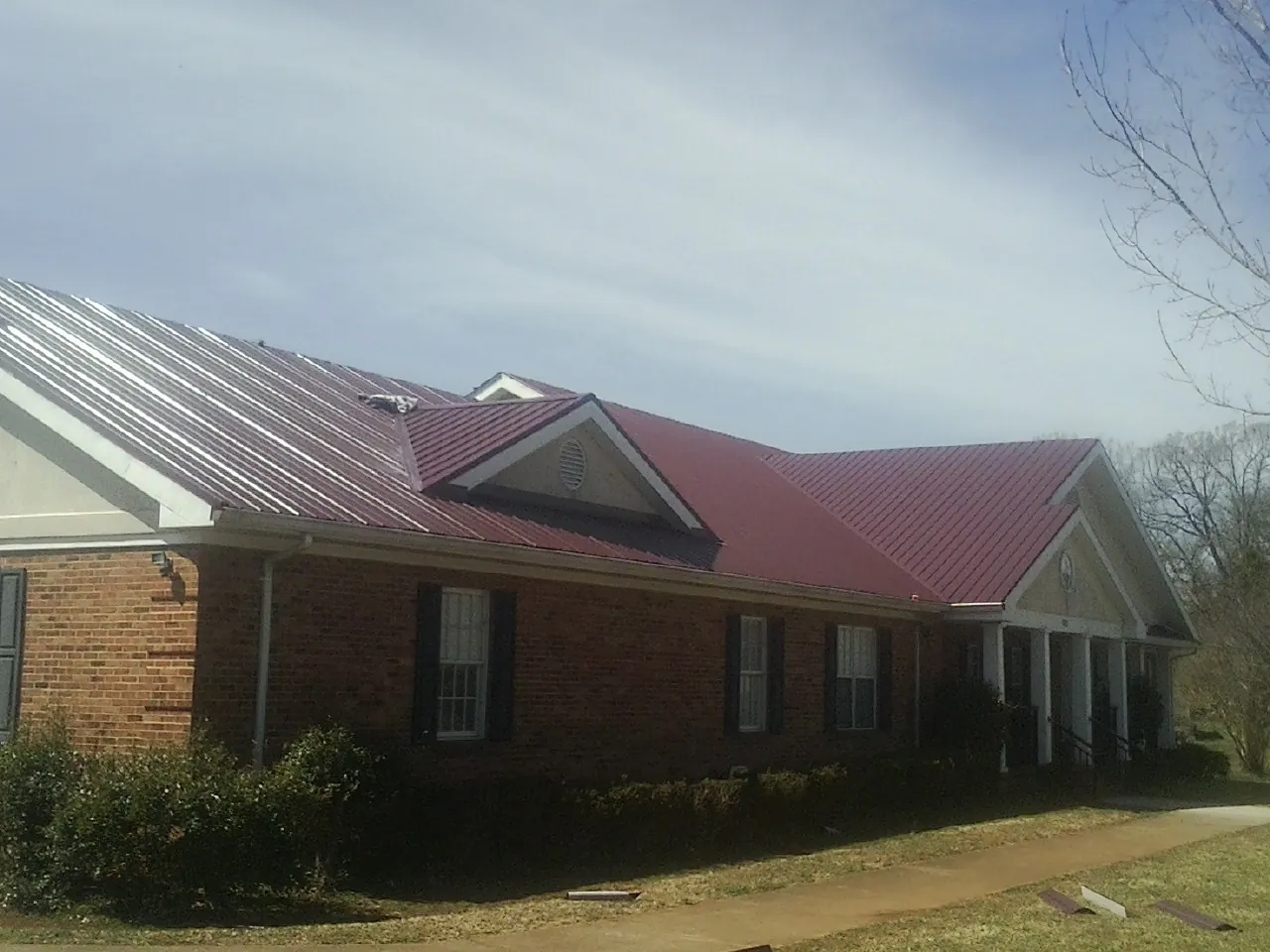 Red metal roof with gabled entries on a long brick building, from a Hail Damage Roof Repair job in Colwell