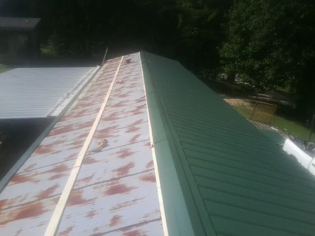 Old rusted panels beside newly installed green metal roofing — Wind Damage Roof Repair by Roofing Brothers in Colwell