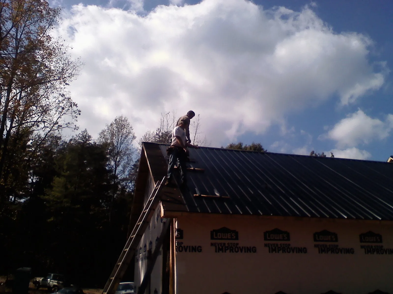 Roofer fastening dark metal panels high against a cloudy sky, from a Roof Inspection job in Colwell