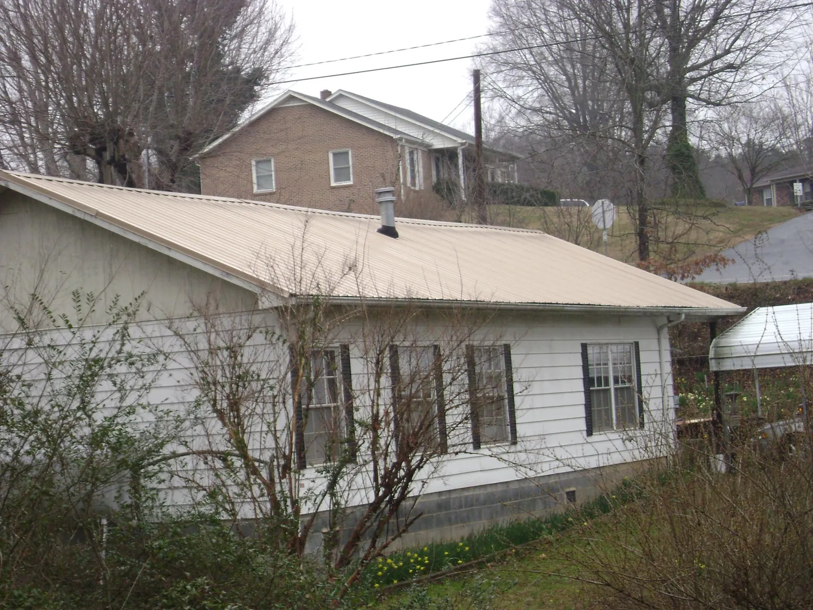 Tan metal roof on a white sided house set into a hillside — Commercial Roofing by Roofing Brothers in Colwell