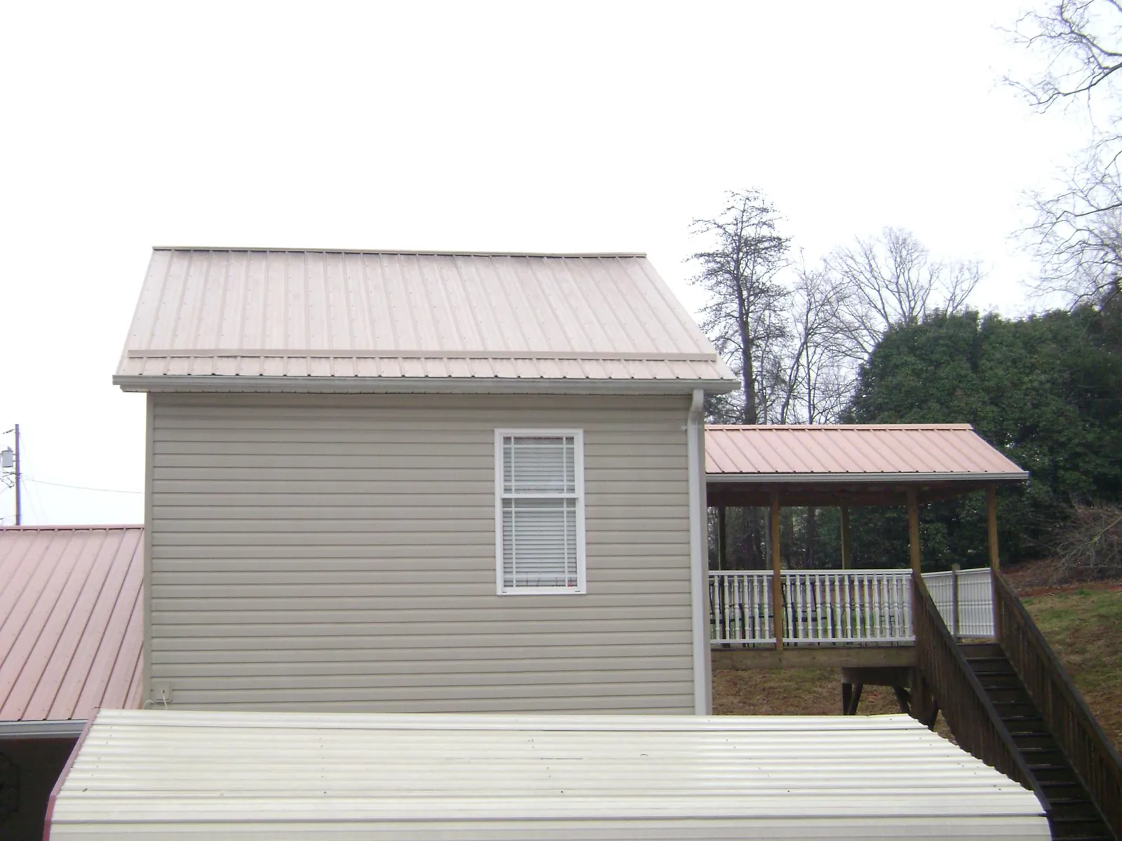 Tan metal roofs on a two story addition and attached porch, from a Roof Replacement job in Colwell